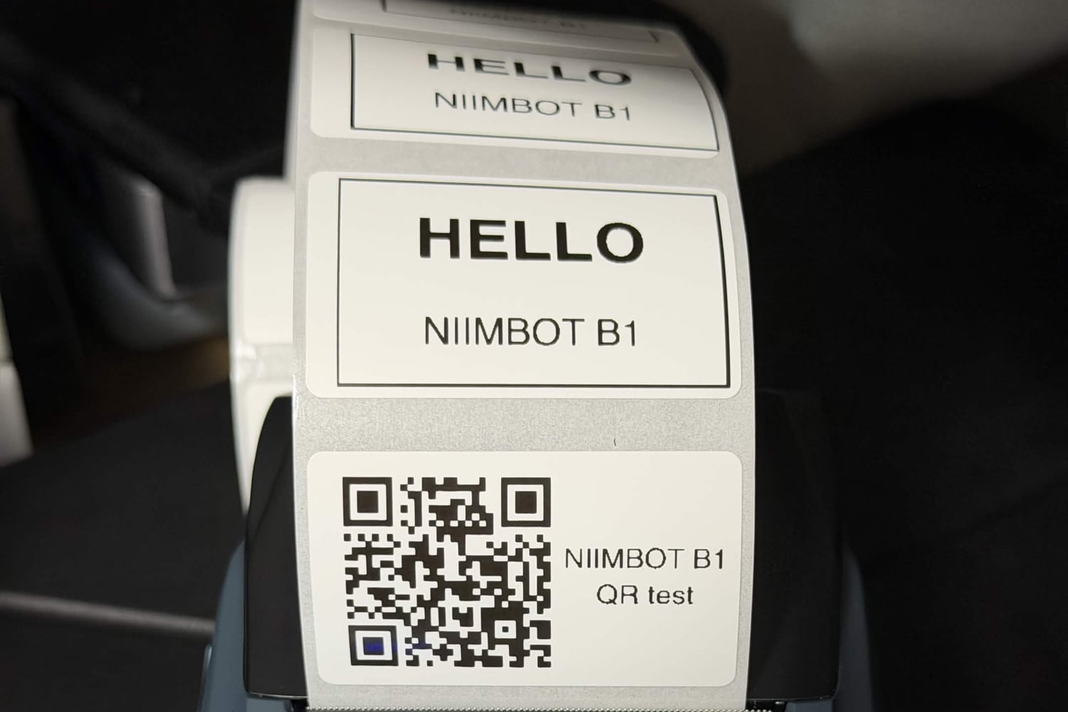 NIIMBOT B1 から出てきたラベル。HELLO と NIIMBOT B1 を書いたテキストのラベルが 2 枚と、niimblue-node のリポジトリの URL を入れた QR のラベルが 1 枚つながっている